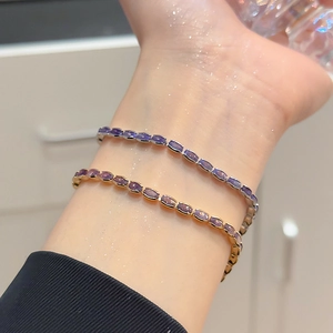 Detailed view of layered silver and gold dainty bracelets with oval purple zircons