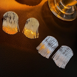 Detailed close-up of metallic tassel earrings with fine woven gold and silver textures