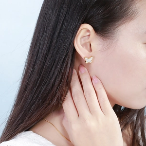 Close-up of golden butterfly stud earrings with white zircon crystals on female model