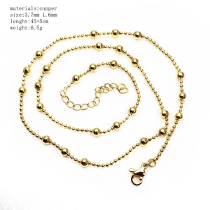 Close-up of golden copper ball chain necklace coiled on white background