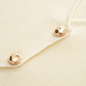 Macro detail of beige knit vest featuring elegant irregular golden metal buttons