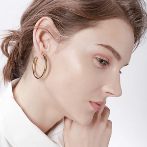 Close-up of model wearing chunky golden C-shaped hollow hoop earrings in polished finish