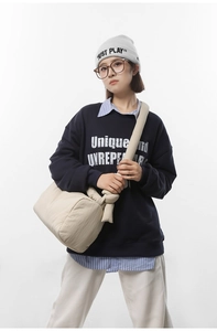 Detail of a beige quilted crossbody bag paired with a navy sweatshirt for a casual look