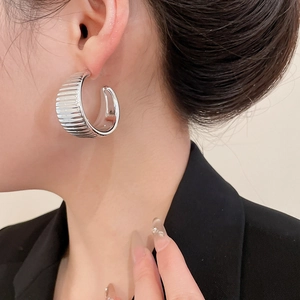 Detail of silver vertical striped C-shape earring showing ribbed metal texture and shine
