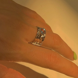 Irregular textured silver ring with moonstone inlay on finger in warm art lighting