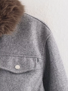 Detailed macro view of the grey wool jacket texture with a brown faux fur collar accent