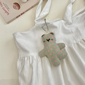 Detail of pink and green checkered teddy bear plush keychain on aesthetic white fabric