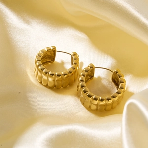 Detail of gold hollow hoop earrings with ribbed texture on luxury silk fabric
