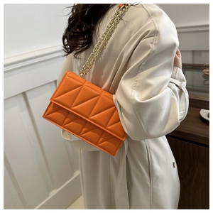 Orange quilted shoulder bag with chunky gold chain strap worn by model in casual setting