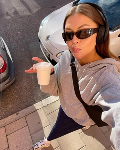 Street style view of retro narrow frame sunglasses paired with a grey hoodie and headphones