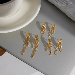 Détail de trois paires de boucles d'oreilles dorées en acier avec pendentifs lune et étoile