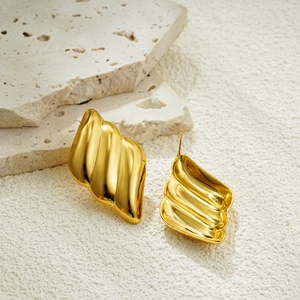 Macro detail of 18K gold plated wing earrings with textured wavy metal surface