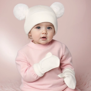 White infant knit hat with double pom-poms and matching gloves set worn by a baby