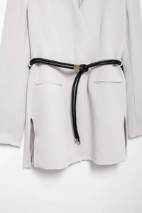 Detail of beige blazer hem with black leather belt and gold buckle in commute style