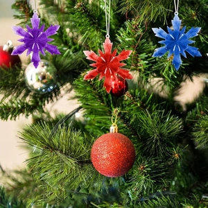 Three snowflake resin ornaments in purple, red, and blue hanging on a decorated Christmas tree