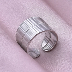 Macro view of textured geometric stainless steel ring on soft pink satin fabric