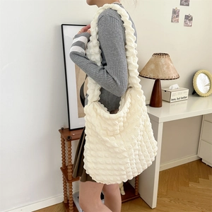 Detail view of large white bubble textured tote bag worn on shoulder in a cozy room