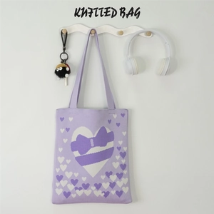Detail of purple knitted tote bag with white heart pattern and coal ball keychain