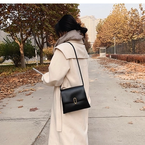 Détail d'un sac à bandoulière en cuir noir minimaliste avec boucle dorée dans une rue d'automne