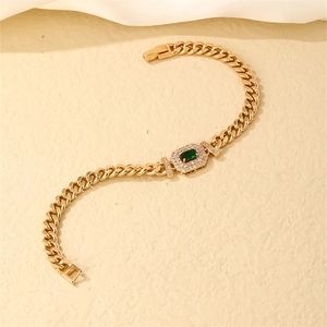 Detail of gold curb link bracelet featuring an emerald green gemstone center and fold-over clasp
