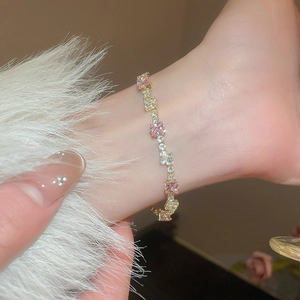 Detailed close-up of a gold bracelet featuring square pink and white zircon stones on a wrist