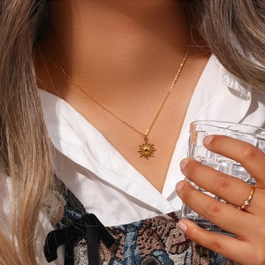 Close-up of a golden sun pendant necklace and delicate ring worn by a model in lifestyle setting