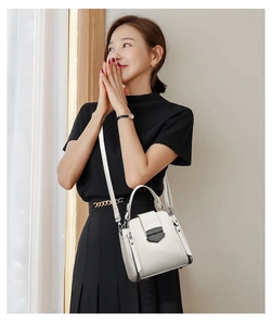 Close-up of white leather handbag with black metal buckle and side zipper detail