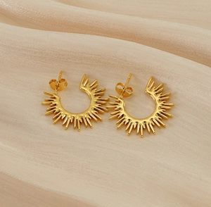 Macro shot of gold sunburst earrings on champagne silk showing intricate spiked details