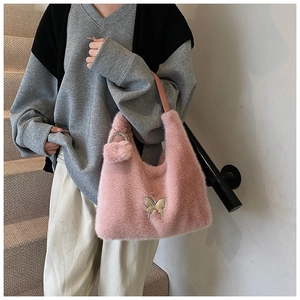 Close-up of pink faux fur bag with silver butterfly metal hardware and plush ball charm