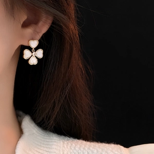 Detailed view of gold-plated clover earrings with white inlay and a central zircon stone