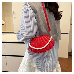 Red shell-shaped crossbody bag with pearl chain shown as a shoulder accessory