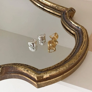 Macro detail of oval sterling silver earrings reflected on a vintage gold mirror surface
