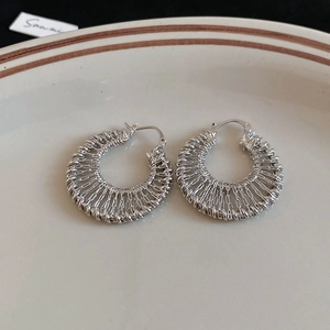 Macro detail of silver woven metal earrings with intricate mesh texture on ceramic plate