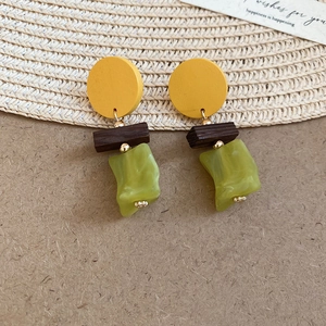Dettaglio di orecchini boho con dischi in legno giallo e pendenti in resina verde su paglia
