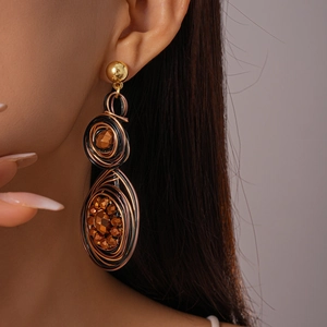 Close-up of handmade gold and black wire-wrapped floral earrings worn by a model