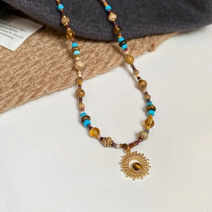 Detailed view of colorful beaded necklace with a gold sun pendant on burlap fabric