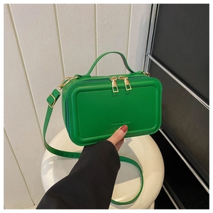 Detail of green suitcase crossbody bag with golden hardware held by a model