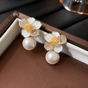 Close-up of golden flower earrings with white enamel petals, rhinestones and large pearl