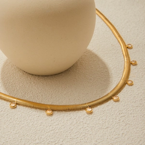 Elegant gold snake chain necklace with round bezel-set crystals on textured surface
