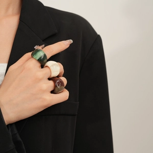 Close-up of wide resin rings in green, cream, and brown on a model's hand