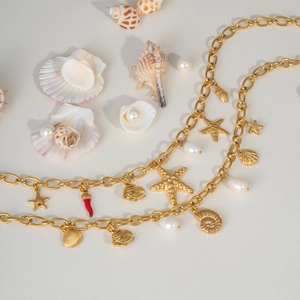 Gold starfish and shell pendant necklace with pearls and chili charms on beige background