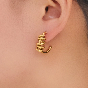 Close-up of golden spiral coil earrings on model's ear showing delicate metallic texture