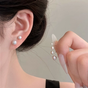 Detailed view of varied sizes freshwater pearl studs worn in a stylish minimalist ear stack