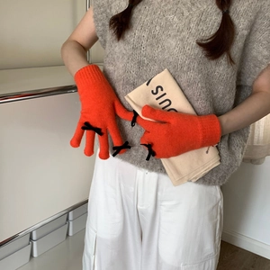 Detail of orange knitted gloves featuring multiple black bows and soft warm texture