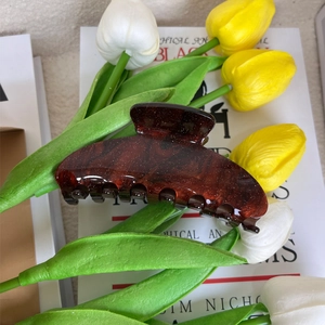 Detailed macro view of amber red hair claw clip with subtle glitter and tulip accent
