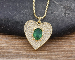 Macro shot of gold plated heart pendant with green gemstone and pavé zircon stones