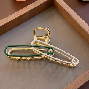Detail of a geometric golden hair claw with green and cream enamel on a display tray