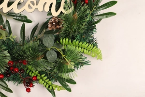 Detail of Christmas wreath with pine needles, red berries, cones and wooden Welcome sign
