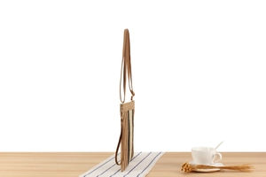 Detailed side view of slim striped woven paper string crossbody bag on a wooden table