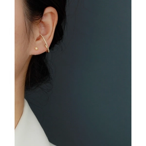 Close-up of gold star stud earring and curved rhinestone ear cuff on model's ear